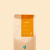 Kaffeepackung aus Packpapier mit orangenem Etikett für den Sumex Blend und den Worten Sumatra, Mexiko sowie 100% Arabica, darunter Symbole für Herdkanne, Siebträger und Vollautomat. Unter dem Etikett das aufgestempelte Blaue Bohne Rösterei-Logo