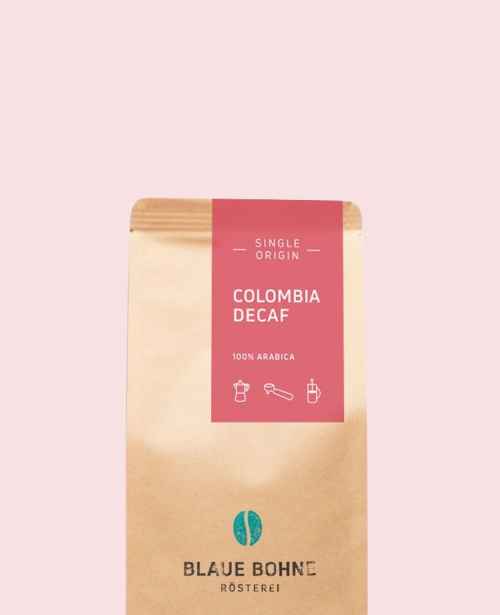 Kaffeepackung aus Packpapier mit pinkem Etikett für den Colombia Decaf Single Origin und den Worten 100% Arabica, darunter Symbole für Herdkanne, Siebträger und French Press. Unter dem Etikett das aufgestempelte Blaue Bohne Rösterei-Logo.