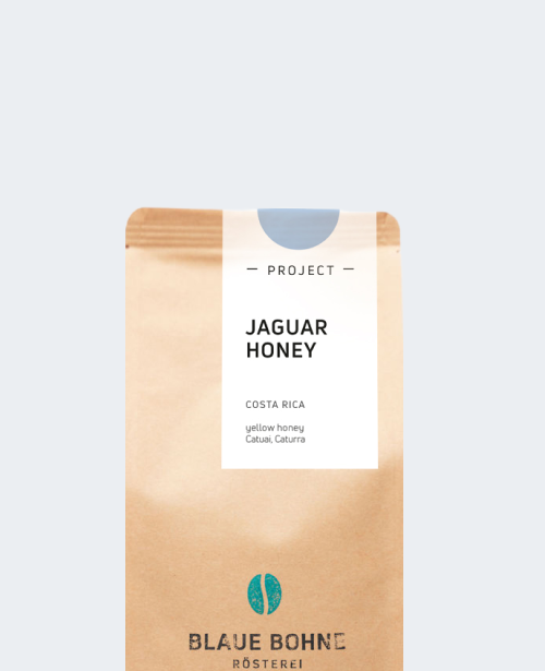 Kaffeepackung aus Packpapier weißem Etikett und leicht Blau oben für den Jaguar Honey Single Origin und den Worten - Project - Jaguar Honey, Costa Rica, yellow honey, Catuai, Caturra. Unter dem Etikett das aufgestempelte Blaue Bohne Rösterei-Logo.