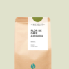 Kaffeepackung aus Packpapier mit weißem Etikett und grünem Kreis oben für den Microlot Flor de Café - Alessandra Single Origin und den Worten Brasilien sowie Natural, Mundo Novo. Unter dem Etikett das aufgestempelte Blaue Bohne Rösterei-Logo.