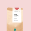 Kaffeepackung aus Packpapier weißem Etikett und Dunkle Pink oben für den Gran Galope Single Origin und den Worten - Single Origin - Gran Galope, Colombia, Washed, Castillo, Caturra. Unter dem Etikett das aufgestempelte Blaue Bohne Rösterei-Logo.