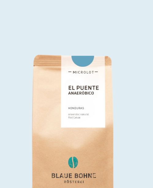 Kaffeepackung aus Packpapier mit weißem Etikett und hellblauem Bogen oben für den El Puente Anaeróbico Microlot Single Origin mit den Worten - El Puente, Honduras, Anaerobic Natural, Red Catuai. Unter dem Etikett das aufgestempelte Blaue Bohne Rösterei-Logo.