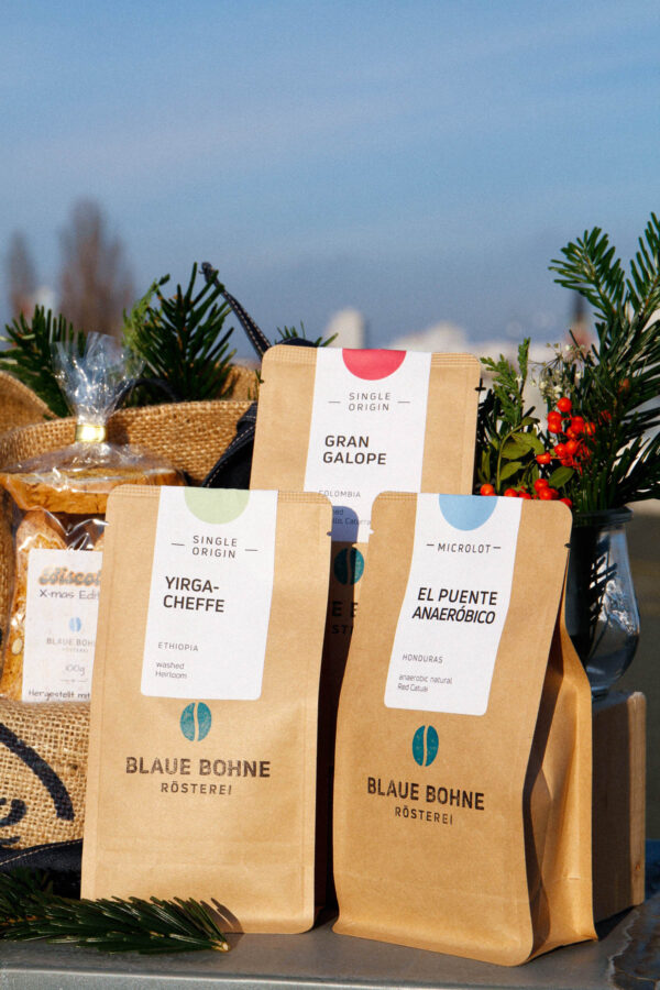 Nahaufnahme des Holy Specials X-mas Coffee Sets von Blaue Bohne mit den Kaffees Yirgacheffe, Gran Galope und El Puente Anaeróbico, umgeben von Biscotti und festlichem Tannengrün.